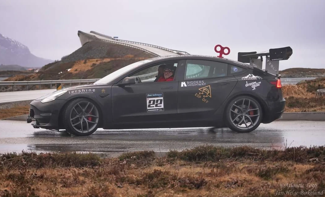 Svart Tesla Model 3 med stor vinge och uppvridningsnyckel på taket vid Atlanterhavsveien i Norge